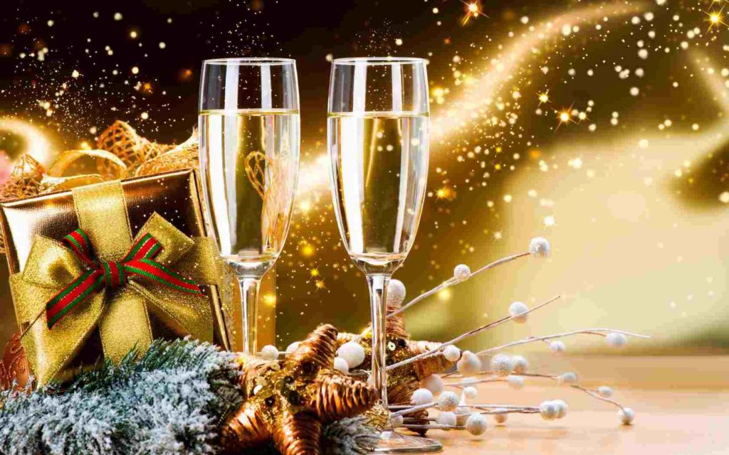 Zlaté pozadie s darčekom s červeno-zelenou mašľou a dvoma plnými pohármi na šampanské.